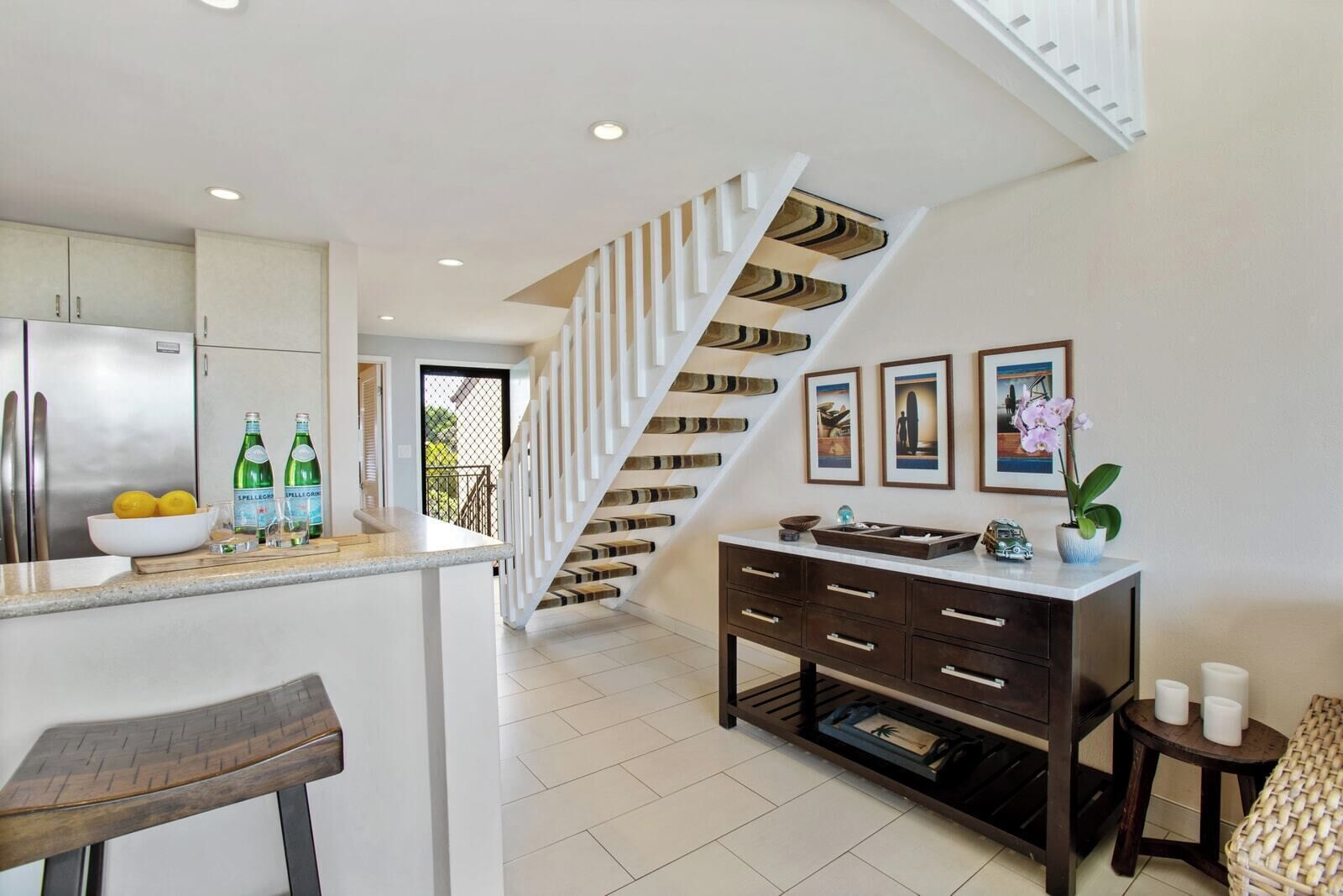 A modern kitchen with a central island, a staircase with a unique design, and a dining area with a bar stool.