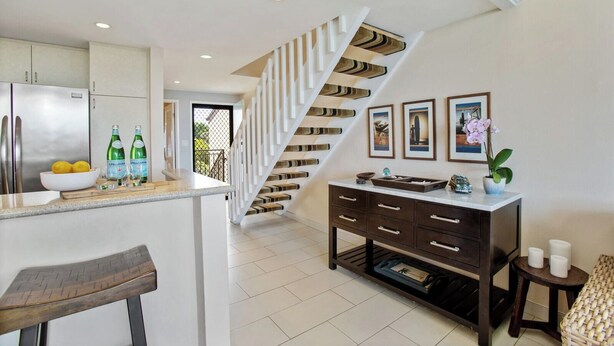 A modern kitchen with a central island, a staircase with a unique design, and a dining area with a bar stool. - Napili Point 2 Water Front Villas, Sleeps 10 | Car Incl. w/ 6 nights | ML-4080 by KBM (Lahaina)