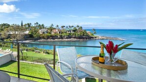 A balcony with a glass table, chairs, a bottle of champagne, and a vase with flowers. - Napili Point 2 Water Front Villas, Sleeps 10 | Car Incl. w/ 6 nights | ML-4080 by KBM (Lahaina)