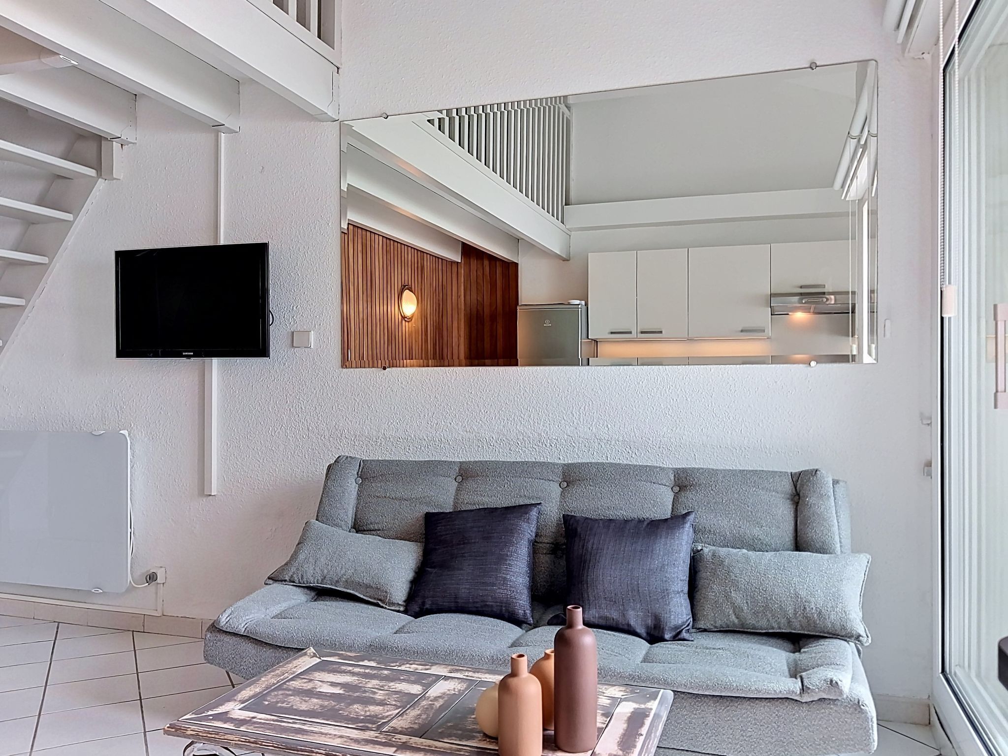 A modern living room with a grey sofa, a flat-screen TV, and a staircase leading to an upper level.