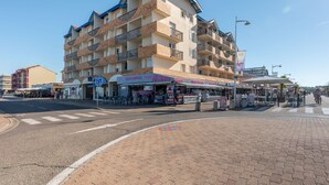 Hotel de varios pisos con balcones, una calle en frente y mesas al aire libre para cafeterías.