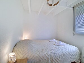 A bedroom with a bed, a bedside lamp, and a window with blinds. - Ortal Océan by Interhome (Lacanau)