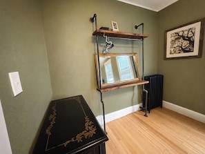 Une pièce avec un plancher en bois, une table noire ornée de motifs floraux dorés, une étagère murale avec un miroir et un radiateur.