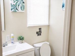 Un baño con inodoro, lavamanos y ventana con persianas.