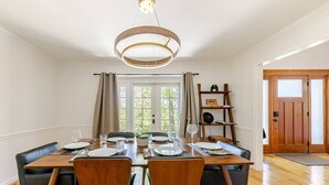 Un coin repas comprenant une table en bois, quatre chaises, un lustre et une vue sur l’extérieur par une fenêtre.