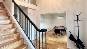 Un escalier avec des marches en bois et des rampes noires, un lustre, un coin repas avec une table et des chaises, et un porte-manteau.