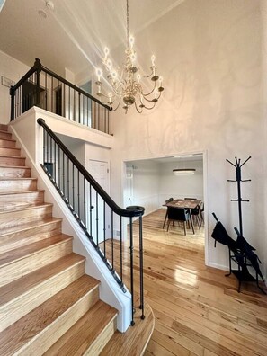 Eine Treppe mit Holzstufen und schwarzen Geländern, eine Kandelaber, ein Essbereich mit Tisch und Stühlen sowie ein Kleiderständer.
