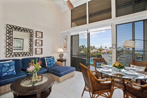 A modern living room with a sofa, dining table, and chairs, large windows with a view, and decorative wall art. - Napili Point 3 Waterfront Villas, Sleeps 16 | Car Incl. w/ 6 nights | ML-4083 by KBM (Lahaina)