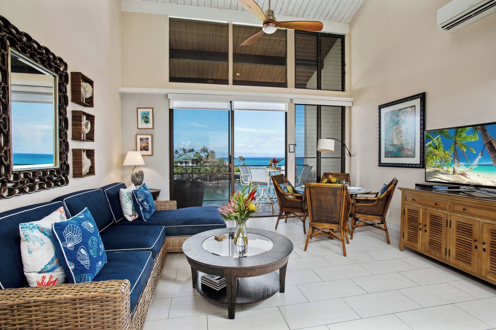 A spacious living area with a sofa, dining table, and chairs, a TV, and a view of the ocean.