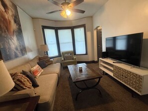 A living room with a sofa, armchair, coffee table, TV, and a ceiling fan.