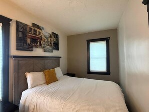 A bedroom with a bed, a headboard, a window, and wall art.