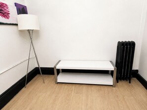 A room with a white floor, a white table, a floor lamp, and a radiator.