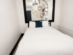 A hotel room with a bed, a large wall clock, and a door.