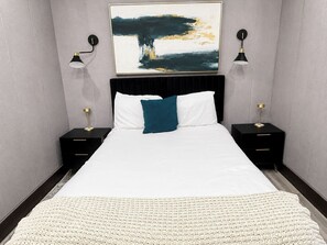 A hotel room with a large bed, two bedside tables, a black headboard, and a wall-mounted abstract painting.