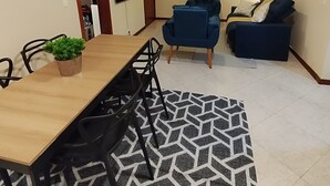 Uma sala de jantar com mesa e cadeiras de madeira, um vaso de planta, um tapete estampado, um sofá azul e um ventilador de teto.