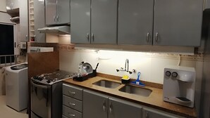 Uma cozinha com armários cinza, um fogão, uma pia e uma cafeteira.
