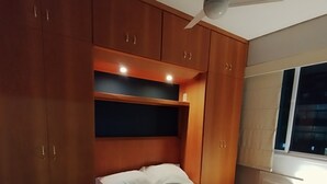 Quarto com cama, ventilador de teto, armários de madeira e janela.