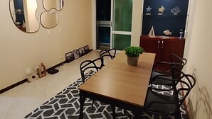 Uma área de refeições com mesa, cadeiras, tapete estampado, planta em vaso e decorações nas paredes.