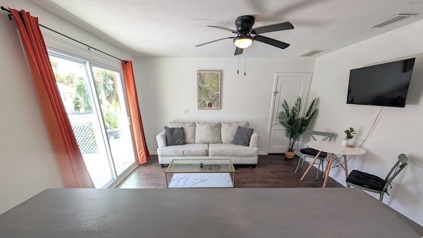 A living room with a sofa, a coffee table, a ceiling fan, a TV, and a sliding glass door. - The Beach Shack | 1BR Getaway (Neptune Beach)