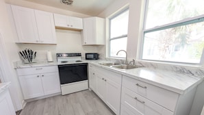 A kitchen with white cabinets, a microwave, a stove, and a sink. - The Beach Shack | 1BR Getaway (Neptune Beach)