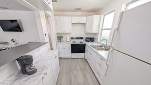 A modern kitchen with white cabinets, a built-in oven, a microwave, and a coffee maker. - The Beach Shack | 1BR Getaway (Neptune Beach)