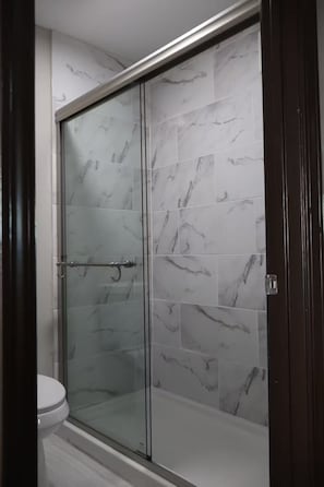 Une salle de bain dotĂ©e dâune douche Ă parois de verre, de carreaux de marbre blanc et dâune porte en bois foncĂ©.