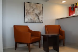 A room with two orange chairs, a round table, and a wall-mounted abstract painting. - Studio 6 Suites (Warsaw)