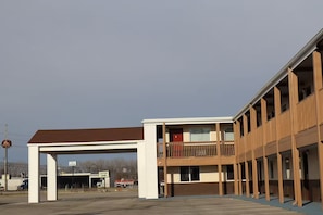 Un motel dotĂ© dâun parking couvert, dâun balcon au deuxiĂšme Ă©tage et dâun panneau indiquant lâentrĂ©e.