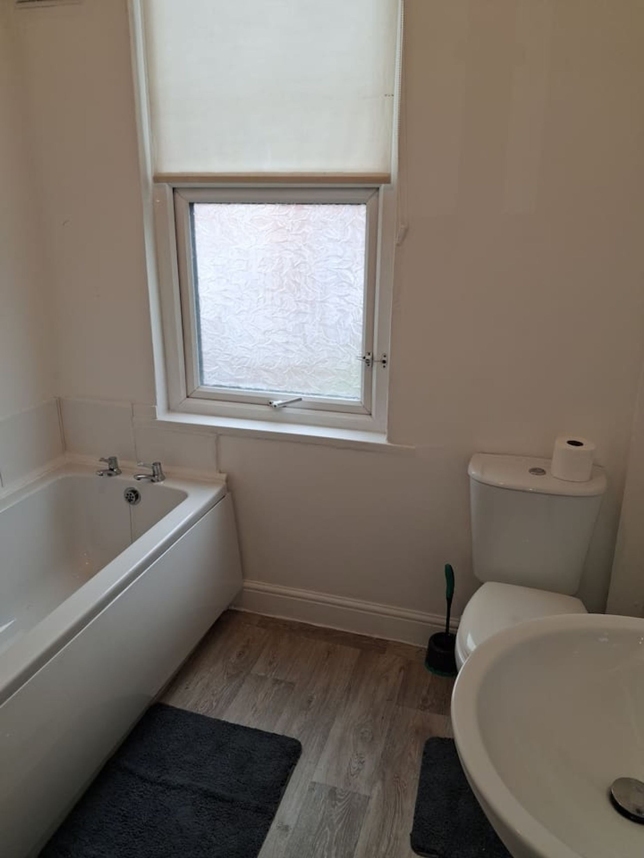 A bathroom with a bathtub, toilet, and sink, featuring a window with frosted glass.