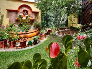 Ein Garten mit Kübelpflanzen, einer Fontäne und einer Backsteinmauer.