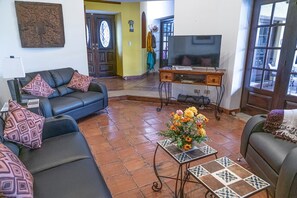 Ein Wohnzimmer mit einer Sofagarnitur, einem Fernseher, einem Couchtisch mit floraler Dekoration und einer Tür mit dekorativer Verkleidung.