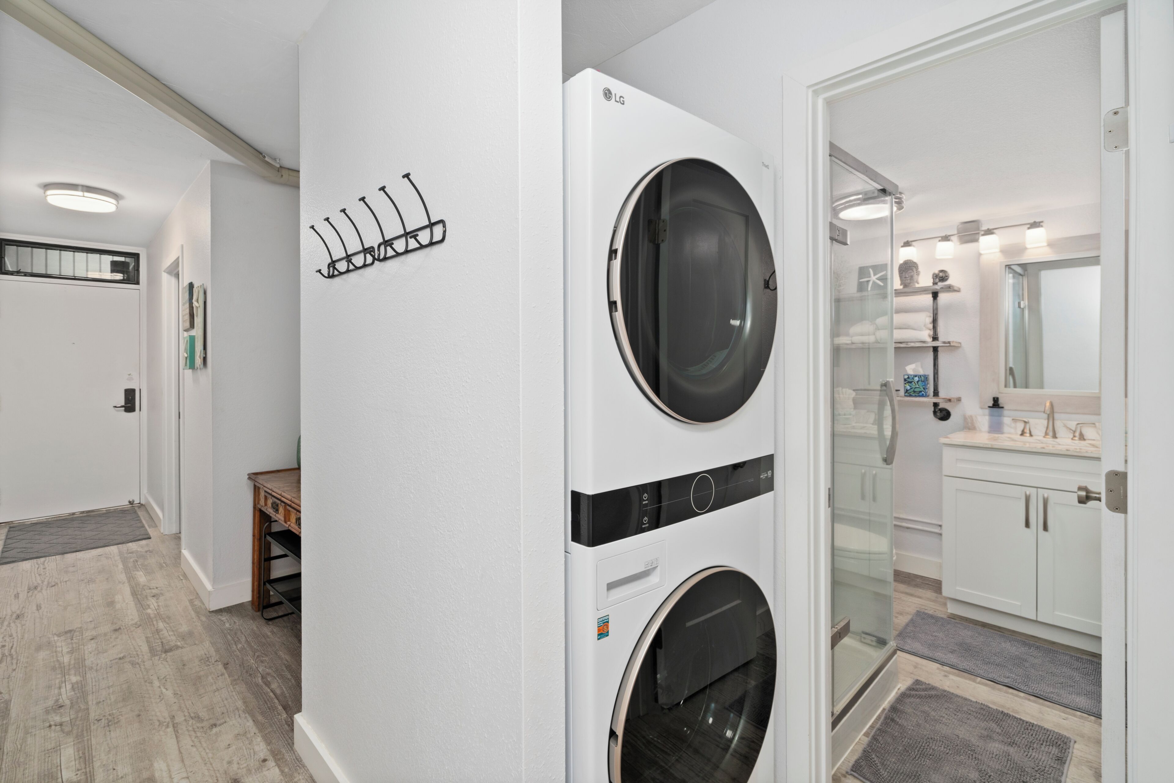 A laundry room with two stacked washers and dryers, a coat rack, and a view into a bathroom with a sink and mirror.