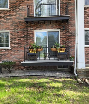 A brick building with a balcony, two potted plants, a small table, and a chair.