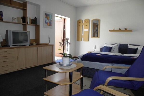 Ein Schlafzimmer mit Bett, Stuhl, Schreibtisch, Fernseher und einem Bücherregal.