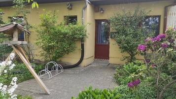 Ein gelbes Gebäude mit roter Tür, ein Garten mit verschiedenen Pflanzen und eine Metallkonstruktion.