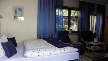 Ein Schlafzimmer mit einem Bett, einem Sessel, einem kleinen Tisch und einem Fenster mit Vorhängen.