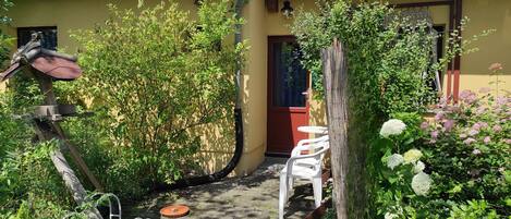 Un jardin avec un chemin dallé, une mangeoire à oiseaux et une petite table accompagnée de sa chaise.