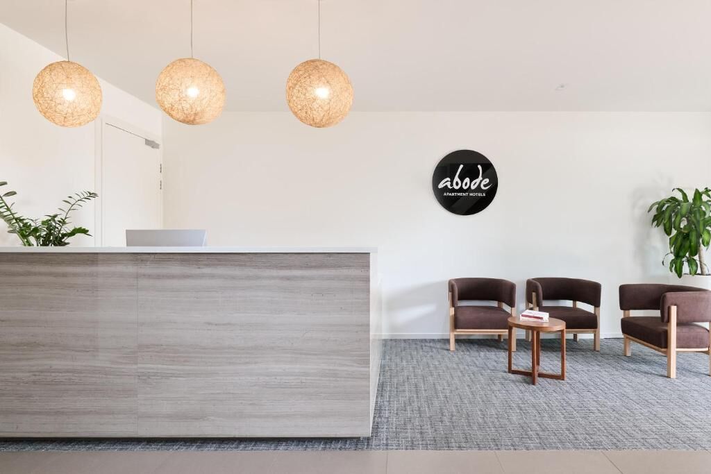 A reception area with a modern desk, three hanging spherical light fixtures, and a sign that reads 'abode apartment hotels.'