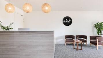 A reception area with a modern desk, three hanging spherical light fixtures, and a sign that reads 'abode apartment hotels.'