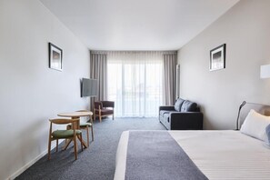 Ein Hotelzimmer mit Bett, Fernseher, Sofa, Sessel und einem kleinen Tisch.