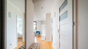 Un couloir avec un banc, une porte et, au fond, on aperçoit une chambre avec un lit et une chaise.