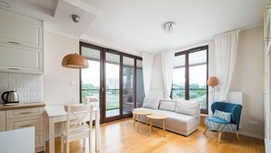 Un salon moderne comprenant un canapé, un fauteuil, une petite table et un coin cuisine avec une bouilloire.