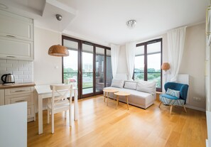 Uma sala de estar moderna com um sofá, uma poltrona, uma mesinha e uma área de cozinha com chaleira.