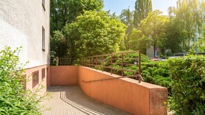 A curved brick pathway leading to a building entrance with a metal railing and greenery. - Grzegórzki Cozy Apartment (Kraków)