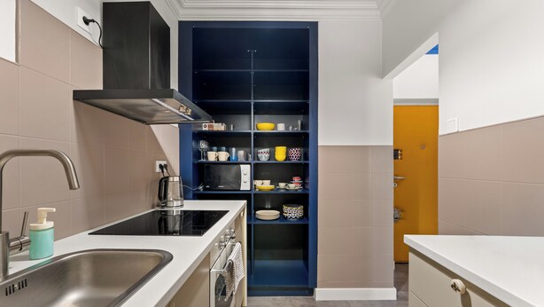 A compact kitchen with a sink, stove, and a blue storage unit with shelves. - Grzegórzki Cozy Apartment (Kraków)
