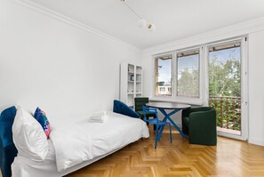 Ein Zimmer mit einem Bett, einem kleinen Tisch, Stühlen, einem Fenster mit Jalousien und einem Balkon.