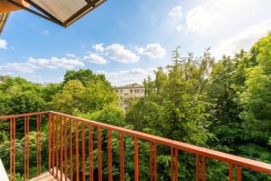 A balcony with a red railing overlooking a lush green landscape and a building in the distance. - Grzegórzki Cozy Apartment (Kraków)