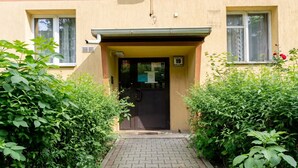 A building entrance with a paved pathway leading to a door, surrounded by dense green foliage. - Grzegórzki Cozy Apartment (Kraków)