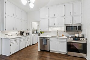 A modern kitchen with white cabinetry, stainless steel appliances, and a wooden floor.