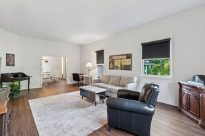 A spacious living area with a sofa, a coffee table, a dining table, and a kitchen area.